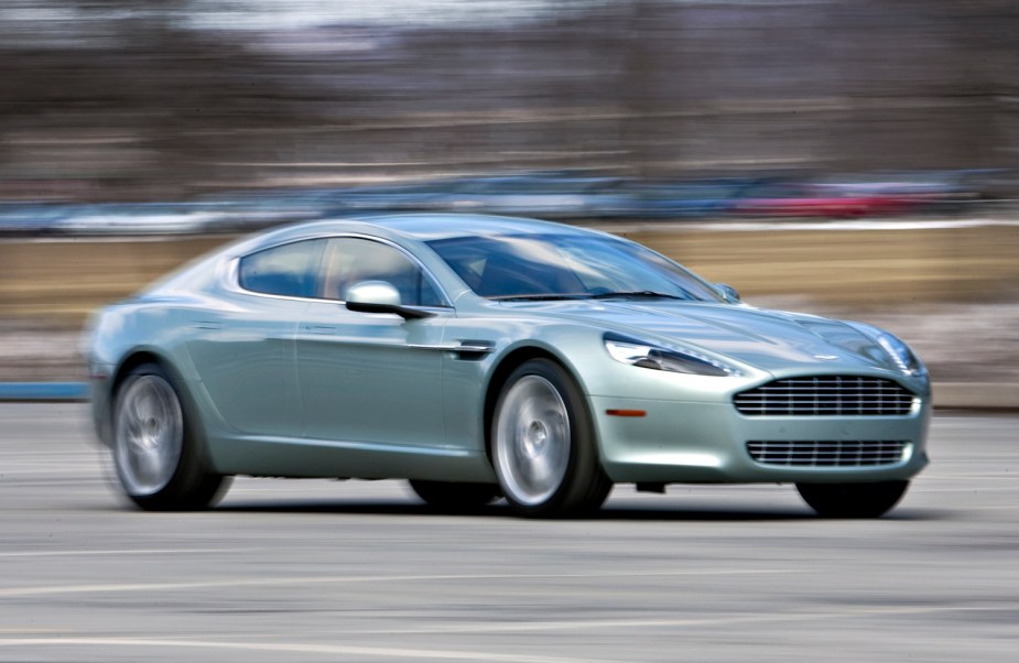 Aqua green Aston Maritn Rapide S sedan with four doors blurs by the camera, a row of parked cars visible in the background.