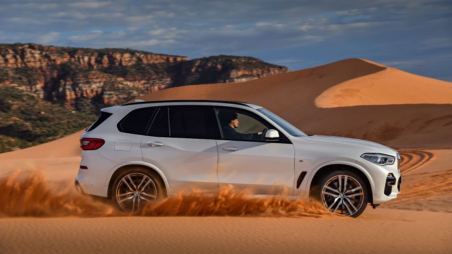 A white A BMW X5 sport activity vehicle (SAV) midsize luxury SUV model driving on sand