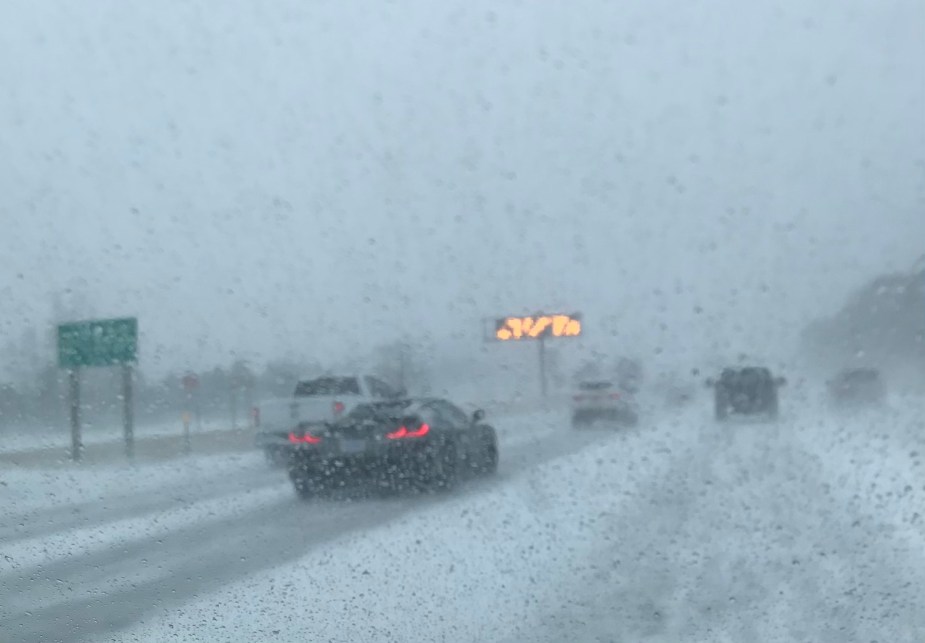 A Corvette cruises down a Detroit highway during a snowstorm with its top down.