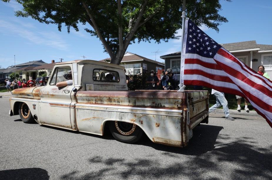 A white dropped vintage pickup truck driving in a parade, an American flag flying in its bed.