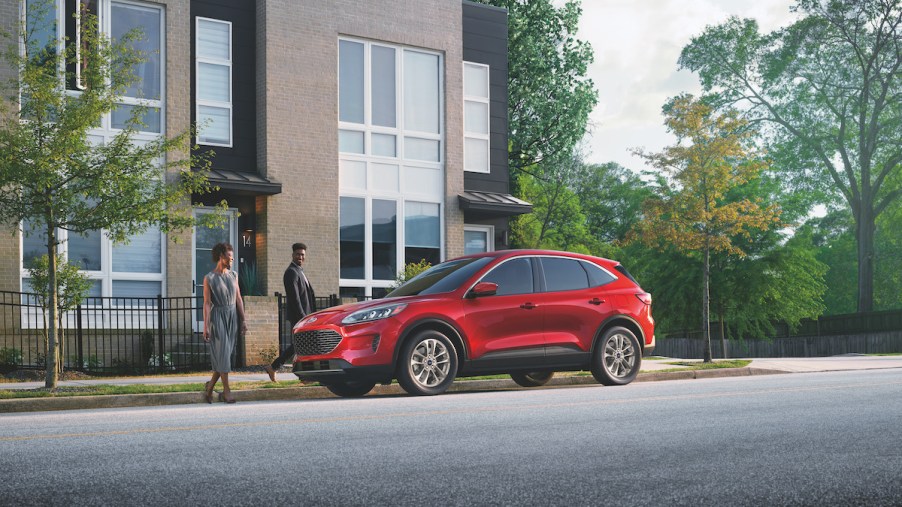 A red Ford Escape, one of the best compact hybrid SUVs to buy, parked in front of a building.