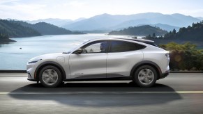 A white 2023 Ford Mustang Mach-E small electric SUV is driving on the road.