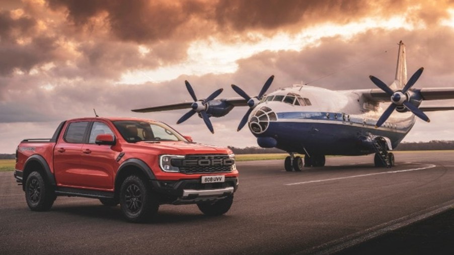 A Ford Ranger Raptor mid-size truck sits in front of a plane.