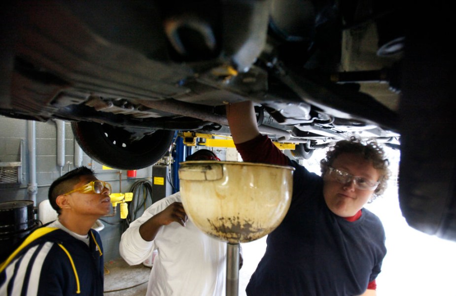 A group of teens changes a car's oil.