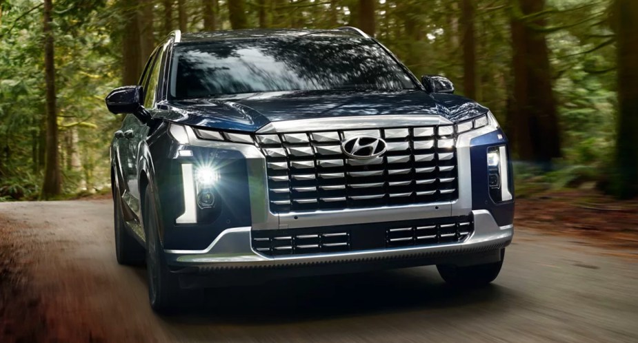 A blue 2023 Hyundai Palisade midsize SUV is driving on the road. 