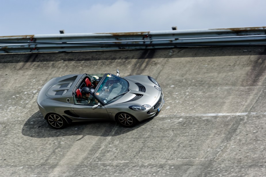 A gray Lotus Elise convertible corners on the steeply banked curves of a race track.