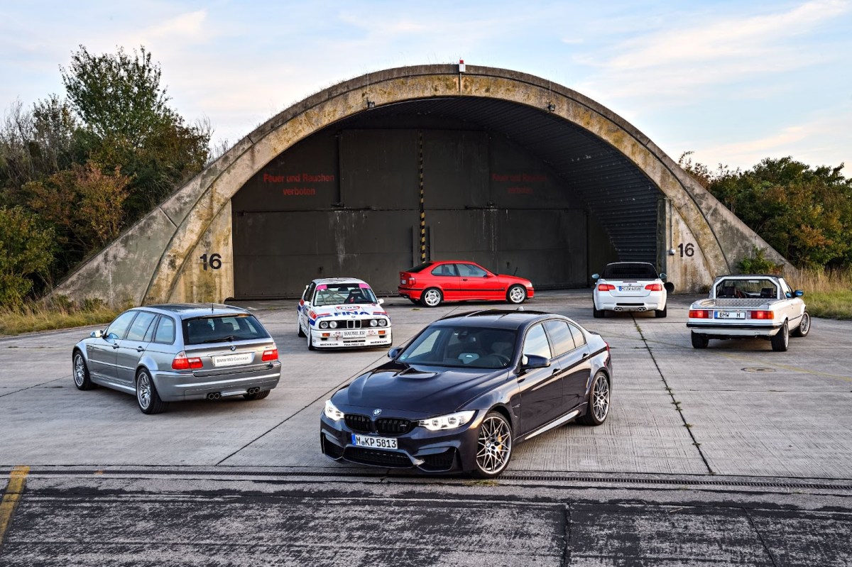 Different generations of BMW M3 parked in front of a hangar