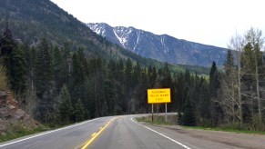 A bright yellow "Runaway Truck Ramp 1 Mile" sign by the side of a road in front of the mountains of Colorado.