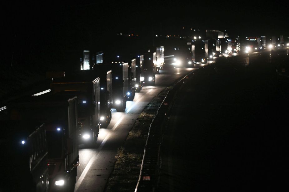 A row of semi trucks waiting in traffic on the interstate highway.