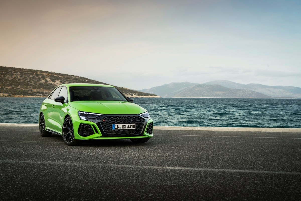A green Audi RS 3 with Quattro parked in front of water and a sand dune
