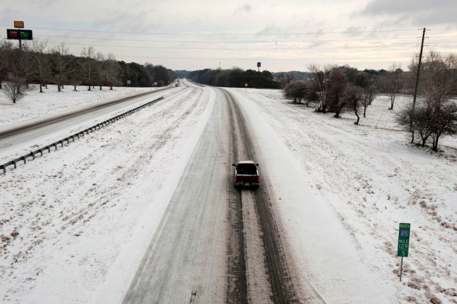 A diesel truck driving down a snowy, deserted interstate on a cold winter day.