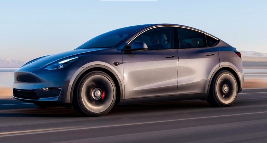 A gray Tesla Model Y small electric SUV is driving on the road. 