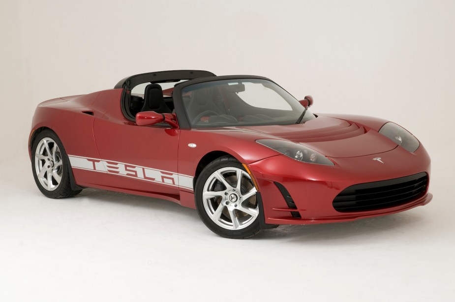 Promo photo of a red Tesla roadster supercar parked in front of a white background.