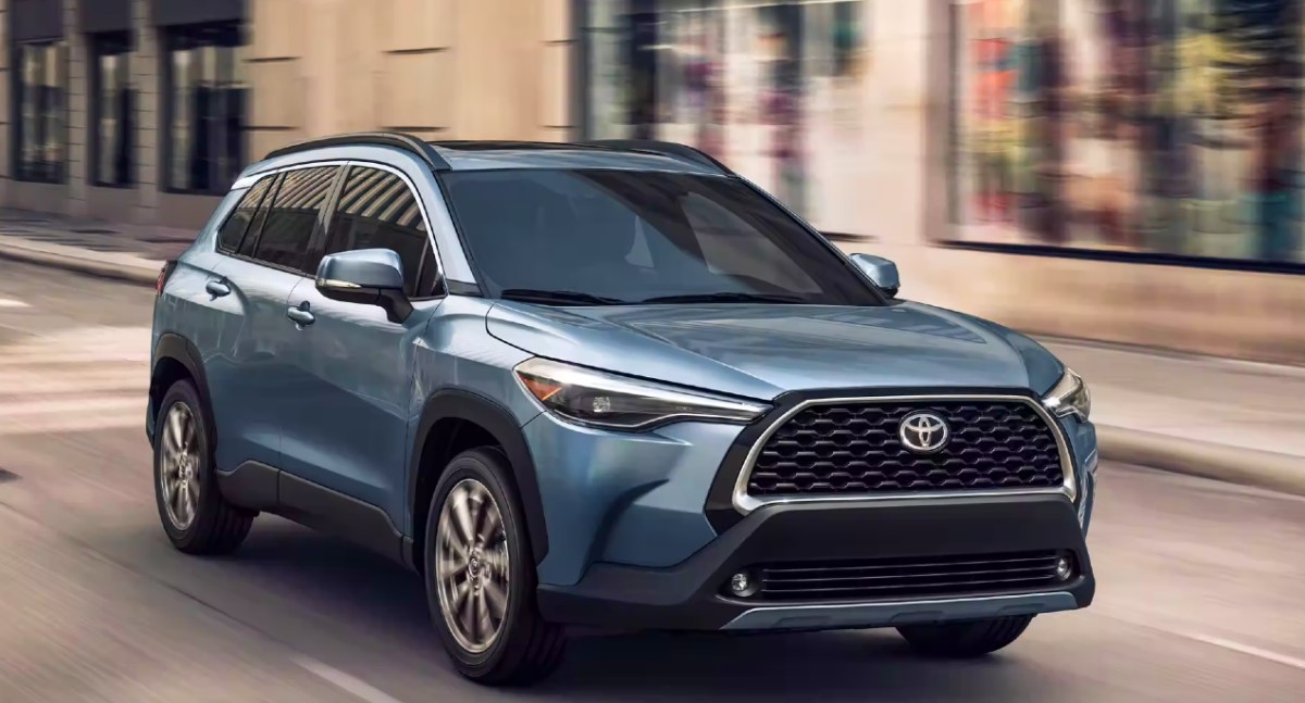 A blue 2023 Toyota Corolla Cross subcompact SUV is driving on the road.