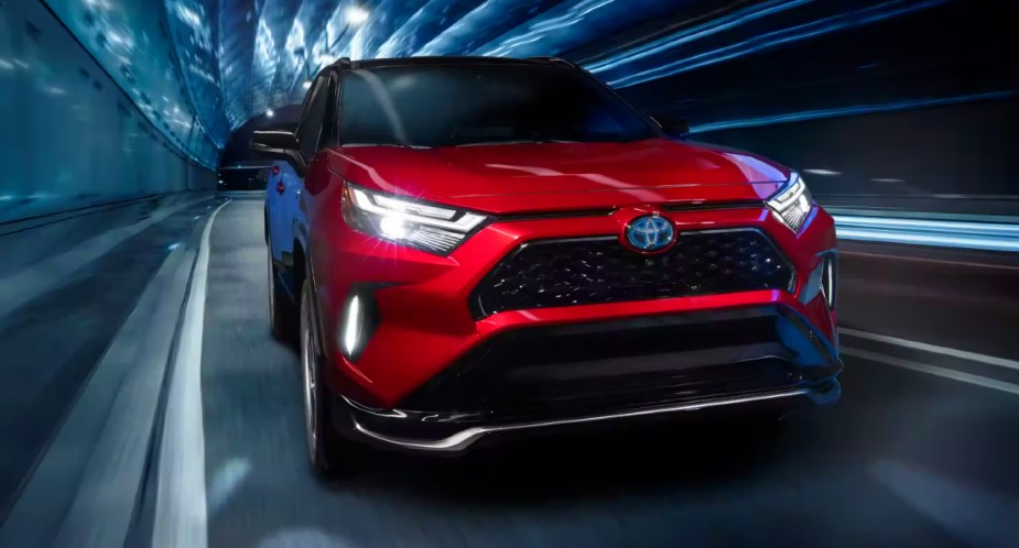 A red 2023 Toyota RAV4 Prime small plug-in hybrid SUV is driving on the road. 