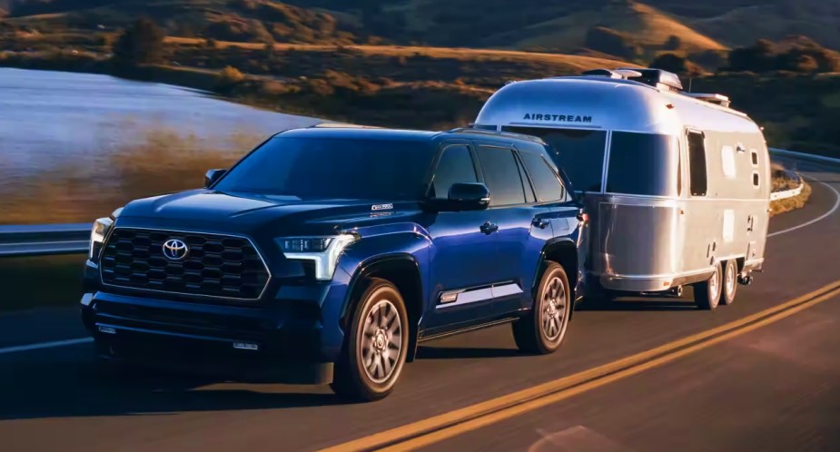 A blue 2023 Toyota Sequoia full-size SUV is towing an airstream trailer on the road. 