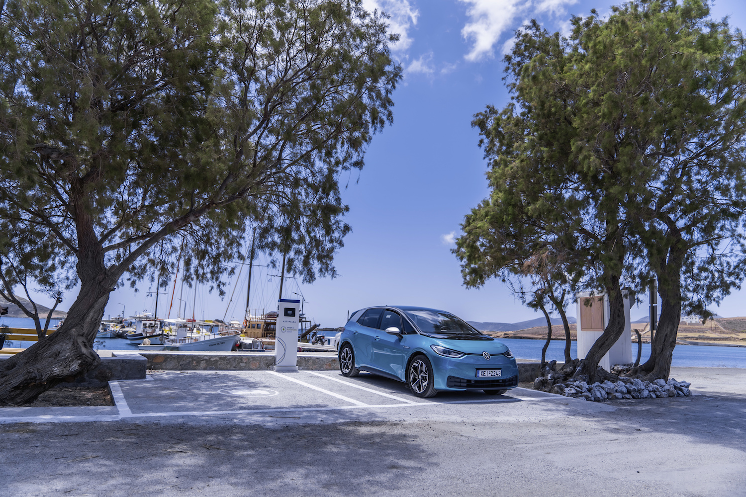 A turquoise Volkswagen ID.4 EV parked in front of the harbor of a greek island.