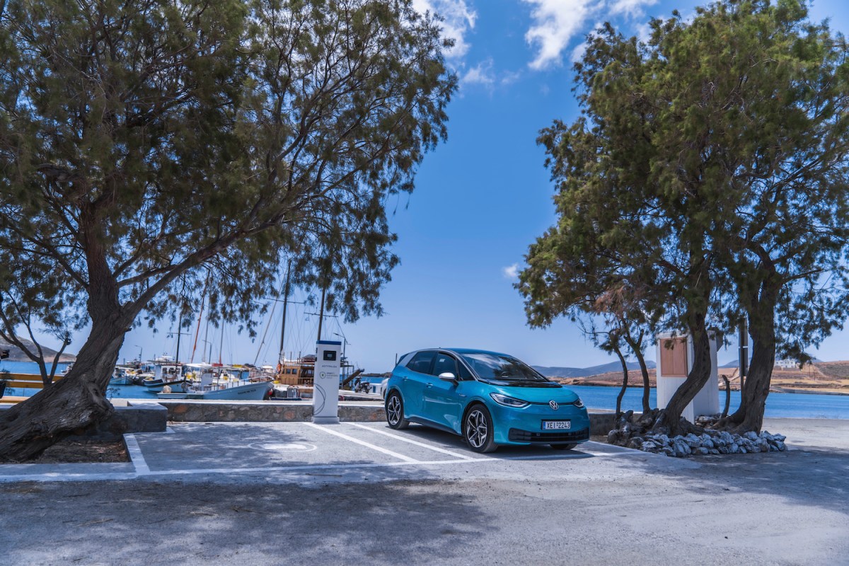 A turquoise Volkswagen ID.4 EV parked outside the port of a Greek island.