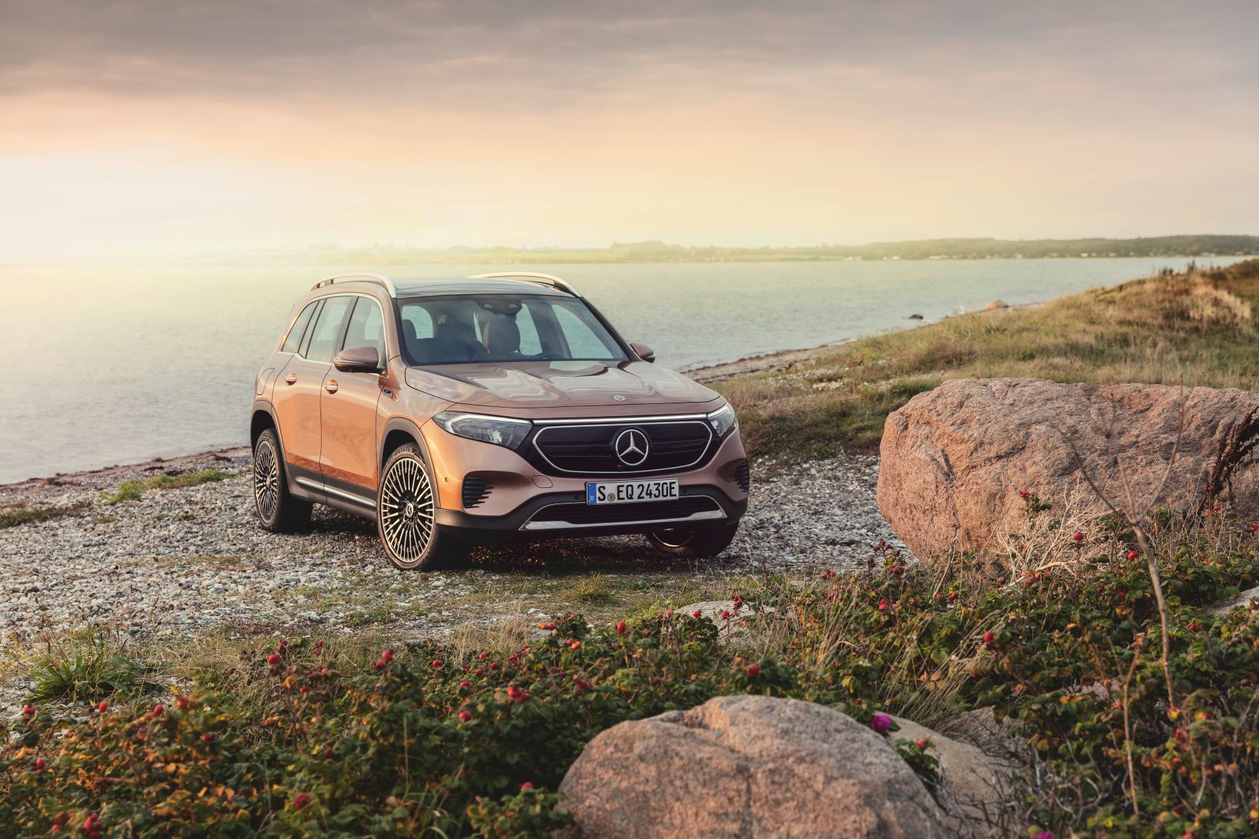 A bronze all-electric Mercedes-Benz EQB SUV parked on a beach near the sea at sunrise