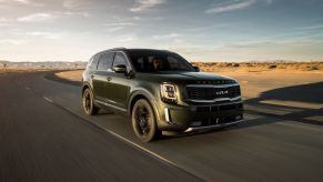 A dark forest green 2022 Kia Telluride midsize SUV driving down a desert highway