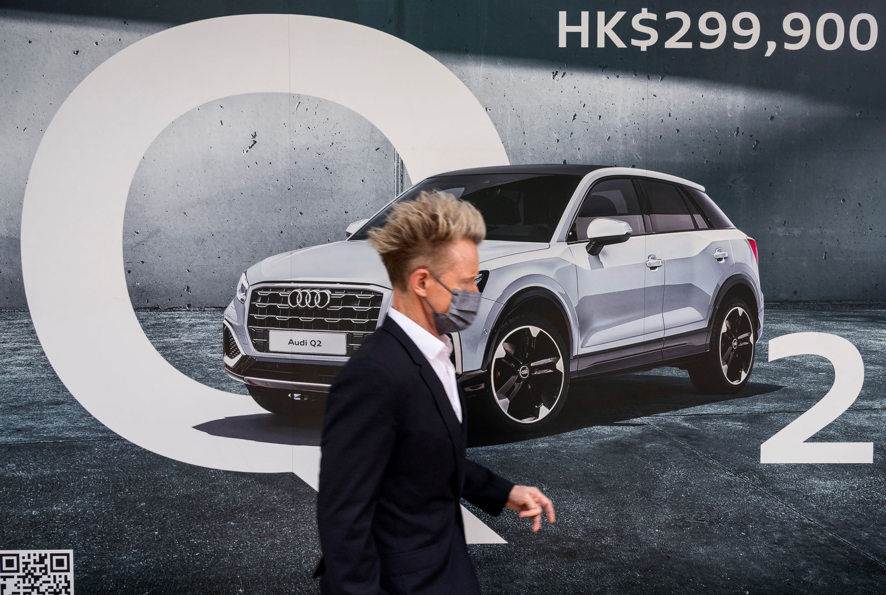 A pedestrian walking past a car advertisement for the Audi Q2 in Hong Kong, China