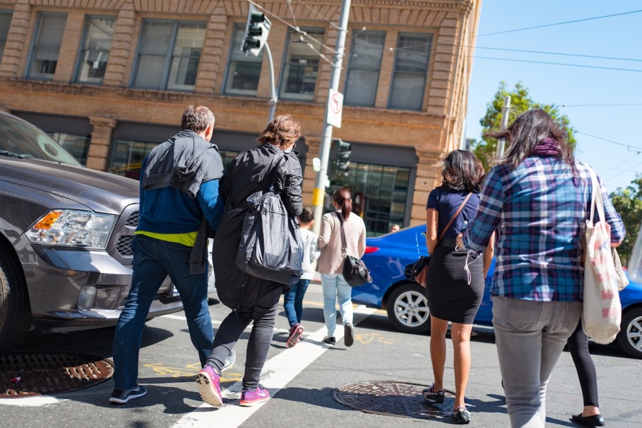 A group of people walk between cars to cross an intersection in San Francisco, California.