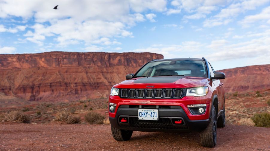 A red 2019 Jeep Compass Trailhawk compact SUV model parked in the desert near red rock hills and cliffs