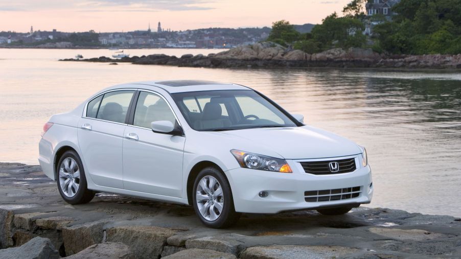 A white 2009 Honda Accord EX-L V6 midsize sedan model parked on rocks near a lake shore