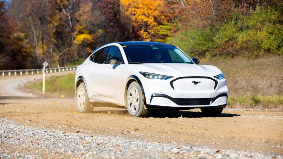 A white Ford Mustang Mach-E all-electric compact SUV model driving on a gravel road