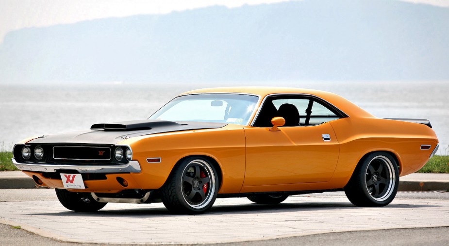 Bright orange 1970 Dodge Challenger parked on pavement, a river visible in the background.