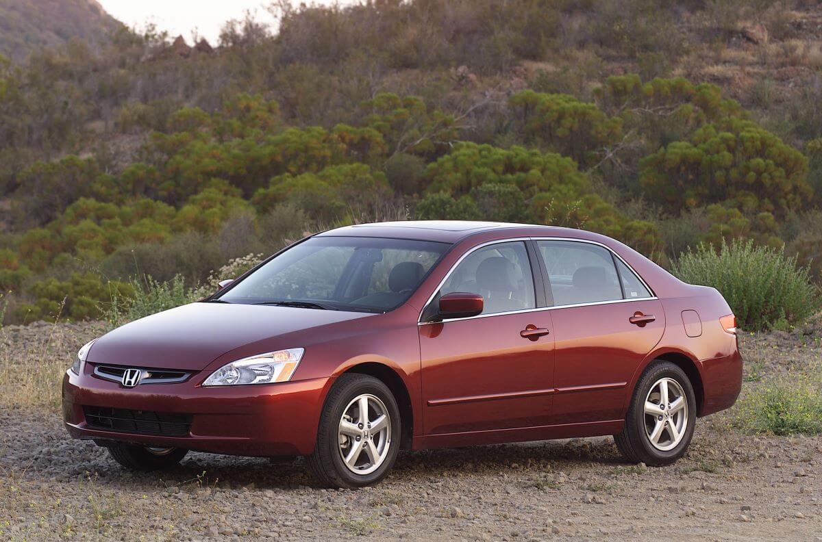 A dark red 2003 Honda Accord midsize sedan model parked on a dirt plain near forest hills. The 2003 model is one of the worst Honda Accord models.