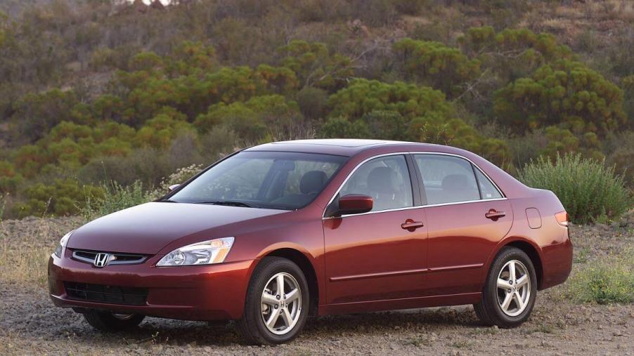 A dark red 2003 Honda Accord midsize sedan model parked on a dirt plain near forest hills. The 2003 model is one of the worst Honda Accord models.