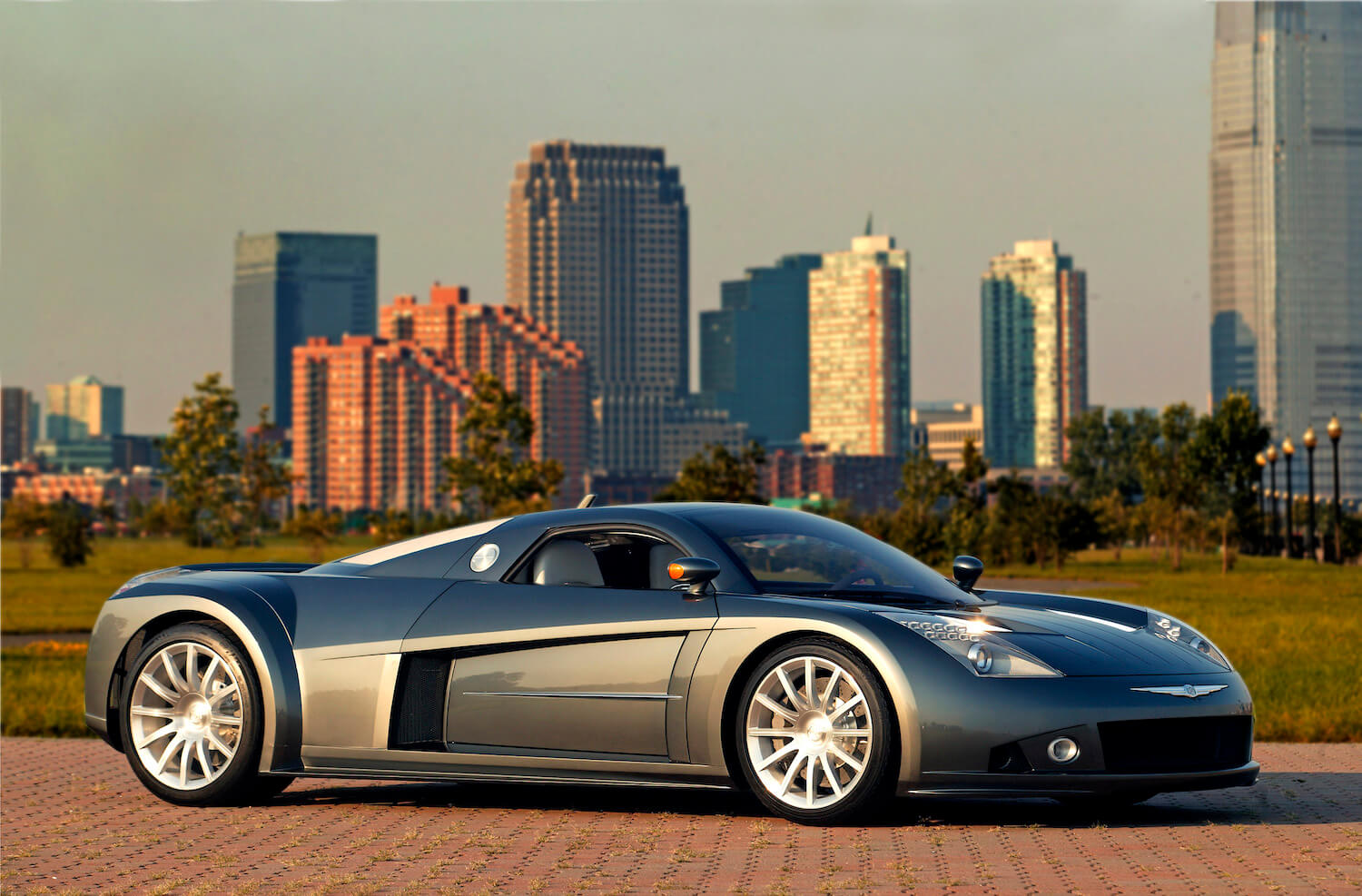 A two seat, mid-engine supercar concept by Chrysler is parked on a cobblestone street, a city's skyline visible in the background.