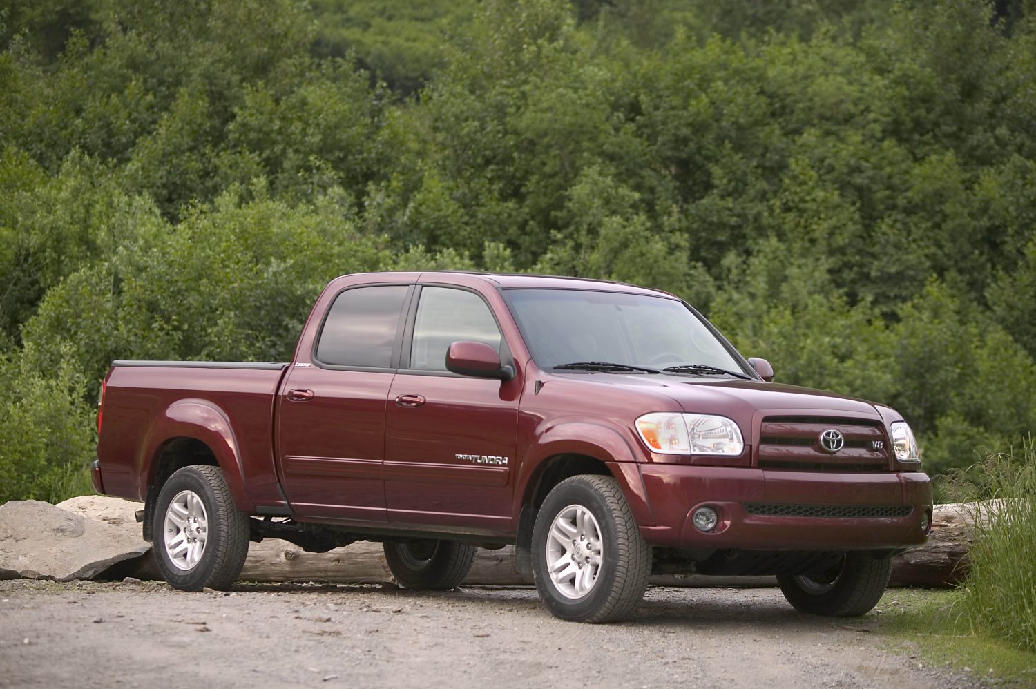 A maroon 2006 Toyota Tundra with a four-door cab parked on a dirt parking lot with green trees in the background.