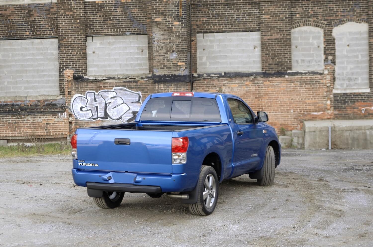 The rear of a blue 2007 Toyota Tundra parked in front of a brick wall with grafitti. 