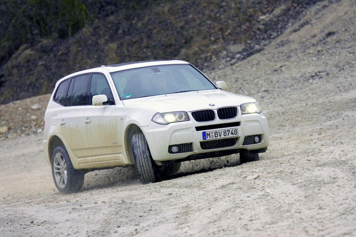 A white 2009 BMW X3 compact luxury SUV model covered in dust and dirt from driving on rocks and gravel