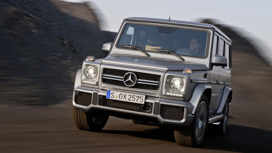 Advertising shot of a 2013 Mercedes G-Class SUV by AMG with a $56k MSRP price driving down a road, the background blurred behind it.