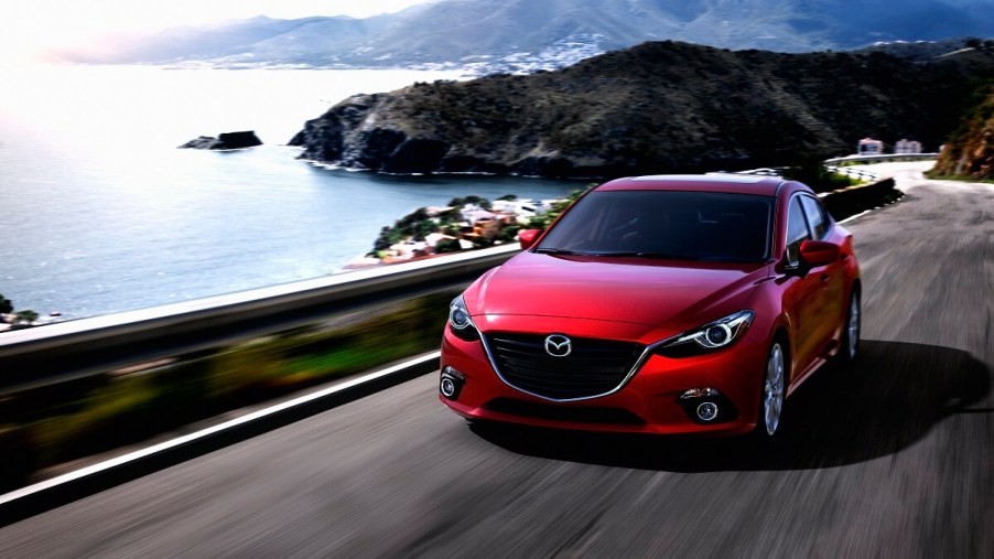 A red 2014 Mazda3 blasts around corners on a coastal road with small car agility.