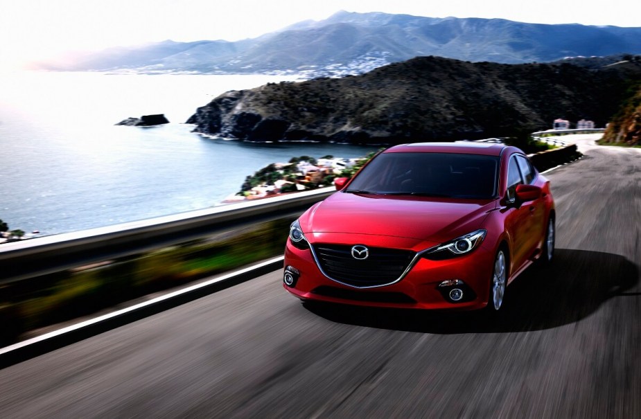 A red 2014 Mazda3 blasts around corners on a coastal road with small car agility. 