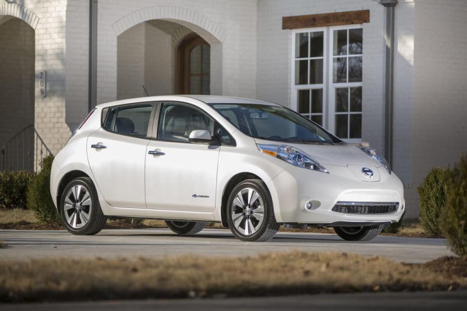 A used white 2015 Nissan LEAF shows off its similar styling to the 2013 model while it parks next to a home.