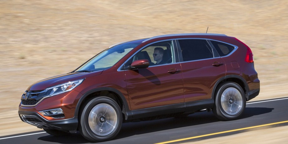 An orange 2016 Honda CR-V small SUV is driving on the road. 