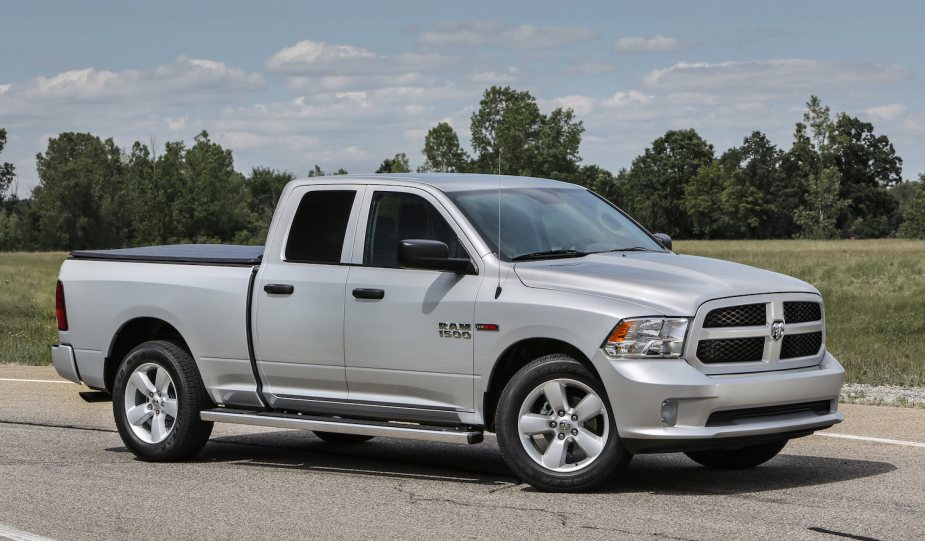 A silver fourth-generation Ram with the cheaper quad cab configuration parked on a deserted road, a row of trees visible in the background.