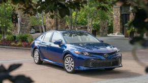 A blue 2018 Toyota Camry LE poses for a picture in a parking lot while showing off its contrast wheels.
