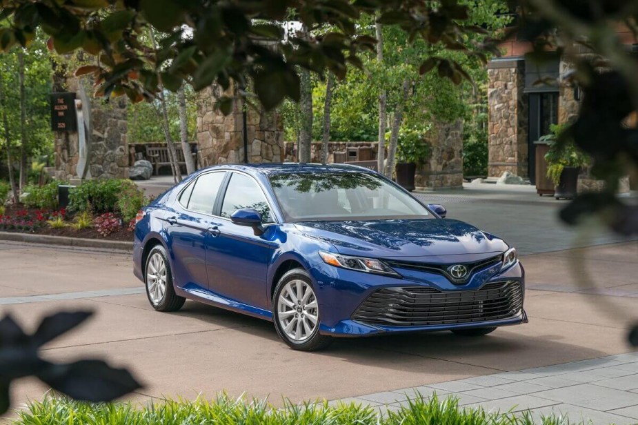 A blue 2018 Toyota Camry LE poses for a picture in a parking lot while showing off its contrast wheels.