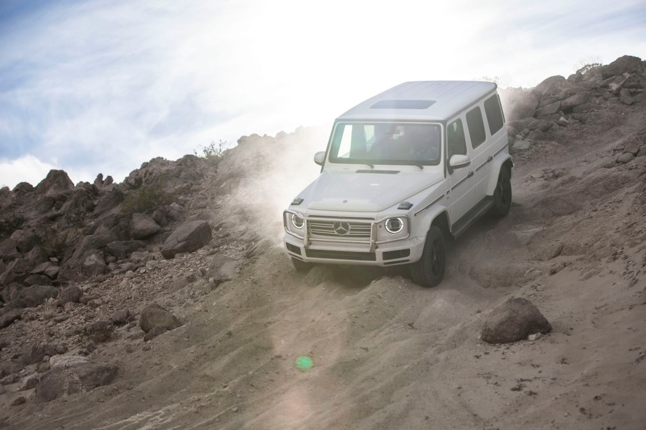 White Merceds Benz G Class descending a rocky hill, blue sky in the background.