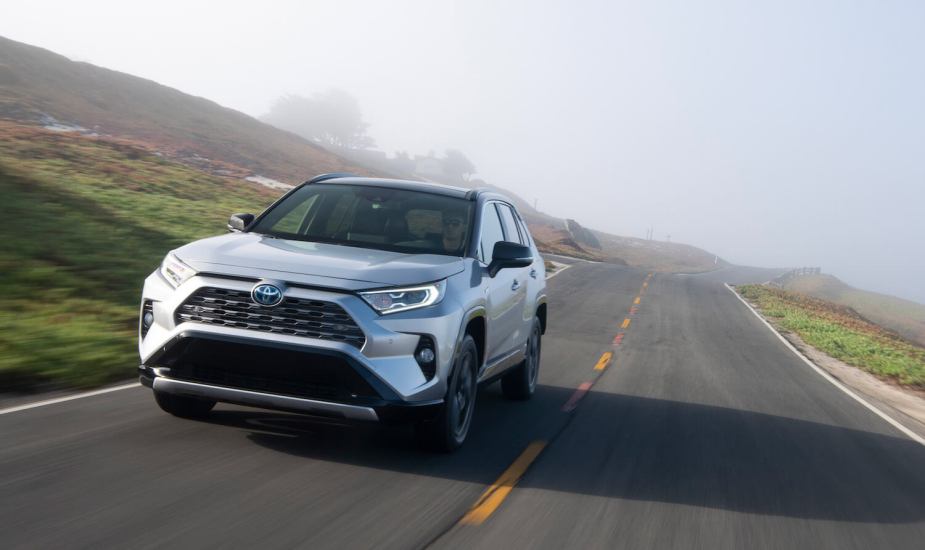 Silver 2019 Toyota RAV 4 Hybrid drives towards the camera, up a country road, fog-covered hills visible in the background.