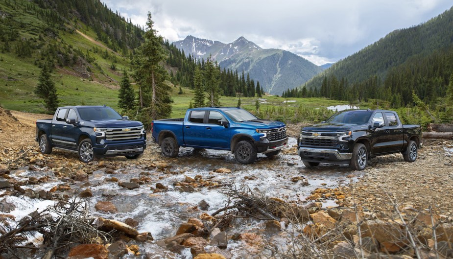 Three 2023 Chevrolet Silverado trucks parked in front of a mountain. 