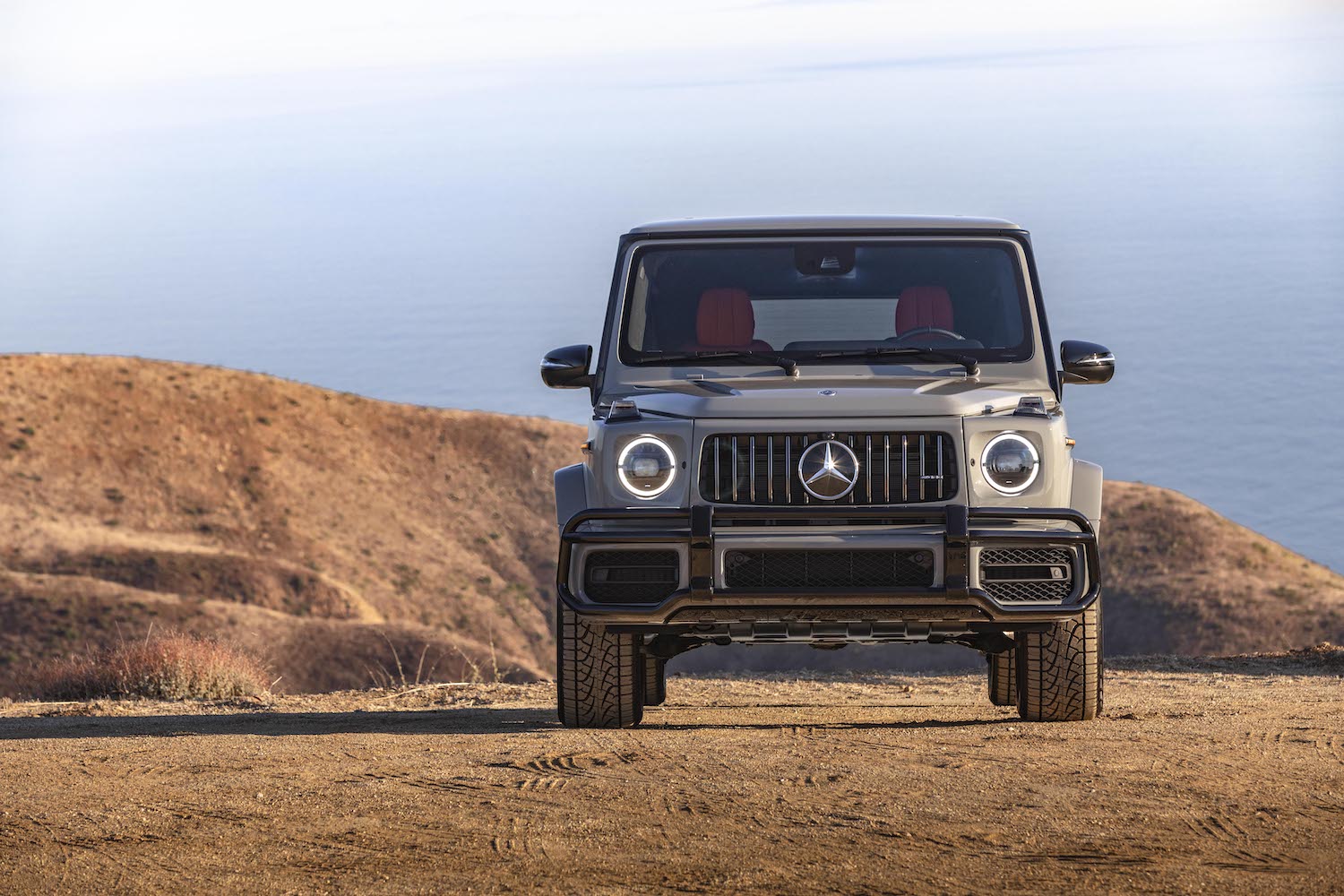 This is a promo photo of a 2021 G Class SUV parked on a sand dune in front of the ocean.