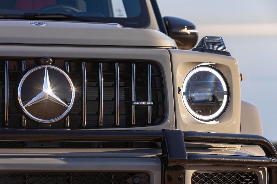 Closeup of a Mercedes-Benz logo on the grille of a tan 2021 G Class SUV with a black AMG brush bar.