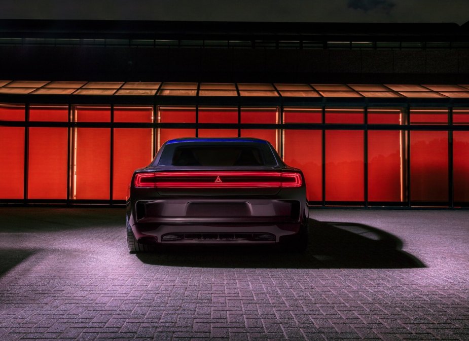 A gray electric Dodge Charge SRT with its tail-light illuminated is parked in front of a red window for a promo photo.